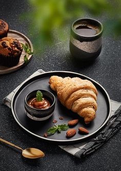 croissants and coffee on a black plate with silverware next to it