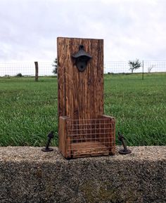 a piece of wood with a wire basket attached to it, sitting in front of a grassy field