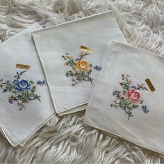 three embroidered napkins with flowers on them sitting on a white furnishing area