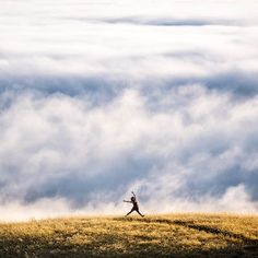 a person running on top of a hill with clouds in the sky behind them,