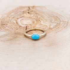 a gold ring with a turquoise stone sits on top of a piece of tree trunk