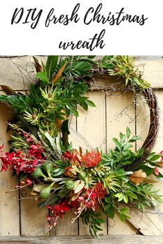 a wreath with red flowers and greenery hanging on a wooden wall next to the words diy fresh christmas wreath