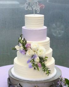 a white wedding cake with purple flowers and greenery on the top is sitting on a table