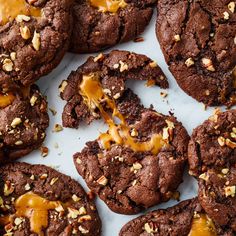 chocolate cookies with caramel drizzle and chopped nuts on top, sitting on a white surface