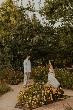 a bride and groom standing in the middle of a flower garden with orange flowers around them