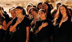 a group of women standing next to each other wearing black dresses and holding wine glasses