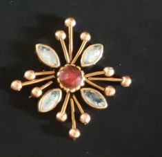 a gold brooch with red and white stones in the center on a black surface