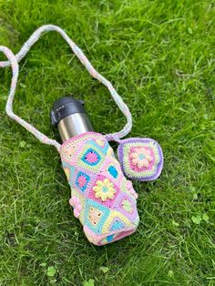 a crocheted camera case laying on the grass with its strap around it's neck