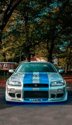 a blue and white sports car parked in a parking lot next to some tall trees