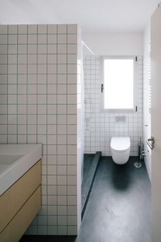 a bathroom with a toilet, sink and window next to it's tiled walls