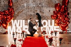 a man kneeling down next to a woman in front of a red carpet with roses on it