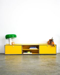 a yellow sideboard with a green lamp on top and books in the bottom drawer