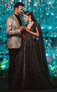 a man and woman standing next to each other in front of a blue wall with lights