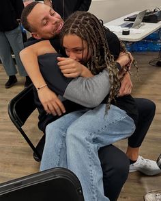 two people hugging each other while sitting in a chair with their arms around one another