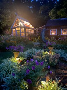 the garden is lit up at night and has purple flowers growing in front of it