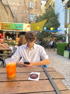 a young man sitting at a table with a drink and cell phone in his hand