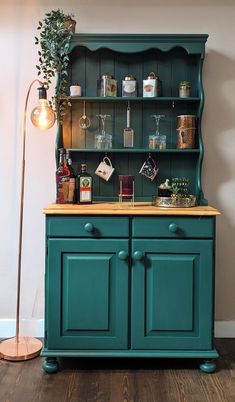 a green cabinet with glass doors and shelves on the top, next to a floor lamp