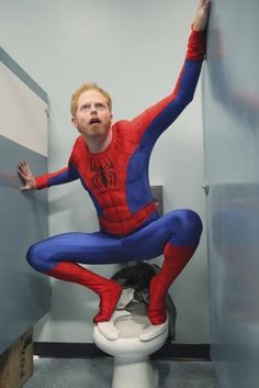 a man in a red and blue suit sitting on a toilet with his arms outstretched