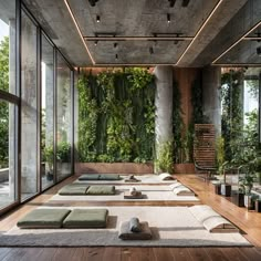 an indoor yoga studio with lots of green plants on the walls and floor, surrounded by large windows