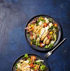 two black plates with chicken, lettuce and tomato salad on blue tablecloth