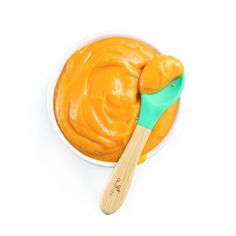 an orange dip in a white bowl with a wooden spoon next to it on a white surface