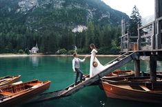 a bride and groom standing on a dock next to some small boats in the water