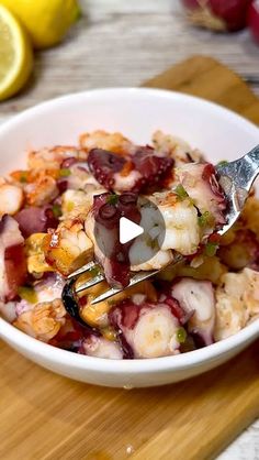 a bowl filled with shrimp and vegetables on top of a wooden cutting board next to sliced lemons