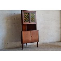 an old wooden cabinet with glass doors on the top and bottom, against a concrete wall