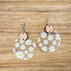 pair of dandeling earrings with white daisies and wooden disc on wood background