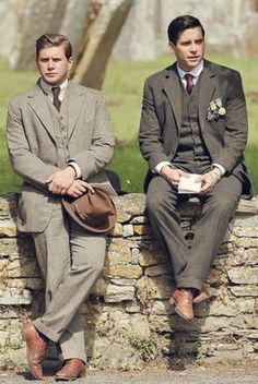 two men in suits sitting on a stone wall