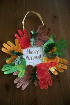 handprinted autumn wreath with happy autumn written in the middle and five hands painted on it