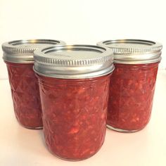 four jars filled with red food sitting on top of a white table next to each other