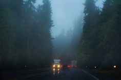 two trucks driving down the road on a foggy day in the woods at night