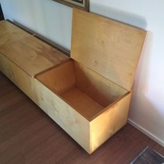 an empty wooden box sitting on top of a hard wood floor next to a wall