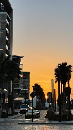 the sun is setting on an empty city street with palm trees in the foreground