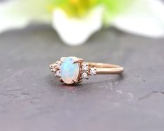 an opal and diamond ring sitting on top of a table next to a flower