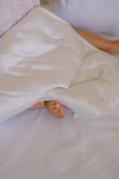 a person laying in bed under a white sheet and pillow with their feet tucked under the covers