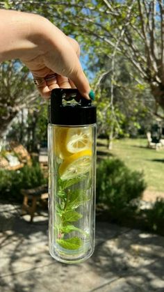 a person is holding a glass with lemons and mint in it while standing outside