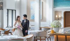 a bride and groom standing next to each other in a room filled with tables and chairs