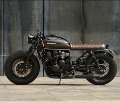 a black motorcycle parked in front of a metal building with a brown leather seat on it