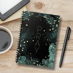 a spiral notebook with the word pray written on it next to a cup of coffee