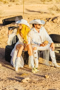 a man and woman sitting next to each other on a dirt road with tires in the background