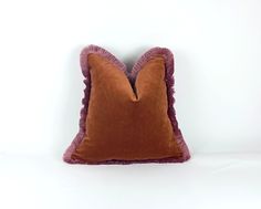 a brown and purple pillow with ruffled edges on a white wall behind the pillows