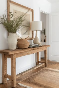 a wooden table with two vases and a lamp on it in a white room