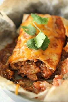 a burrito with meat, cheese and cilantro on it in a bowl