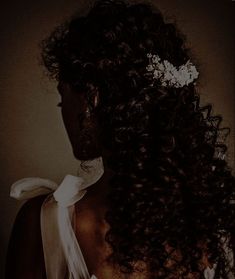 the back of a woman's head with curly hair and a flower in her hair