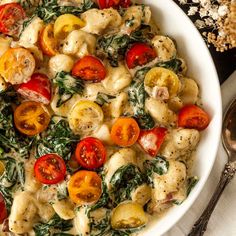 a white bowl filled with pasta, tomatoes and spinach on top of a table