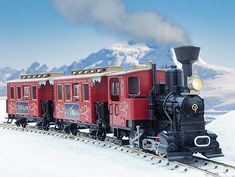 a red and black train traveling through snow covered mountains