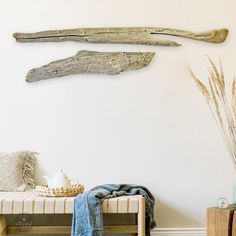 three driftwood pieces hanging on the wall above a bench with a blanket and vase