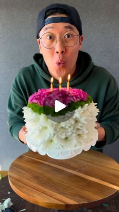 a man blowing out candles on a cake with white and pink flowers in front of him